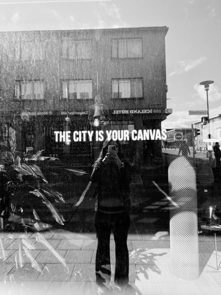 a selfie looking in the mirror on the city street with the wall saying "the city is your canvas"